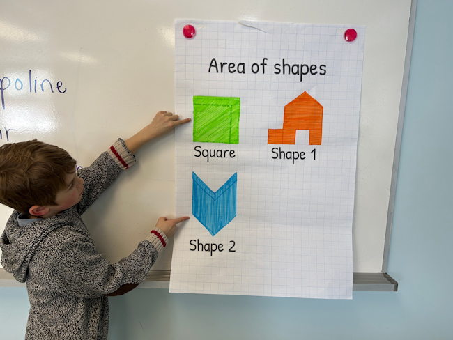 A student is at the board presenting a poster on shapes.